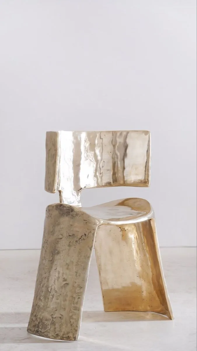 Polished cast bronze chair with a curved back and rough textured legs on a pale floor