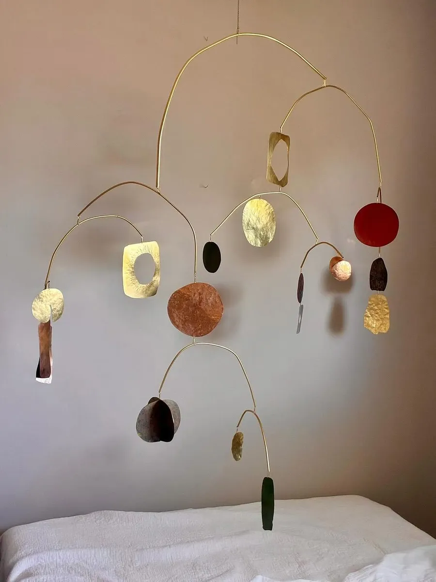 Hanging mobile of hammered brass, copper and one red disc above a white bed