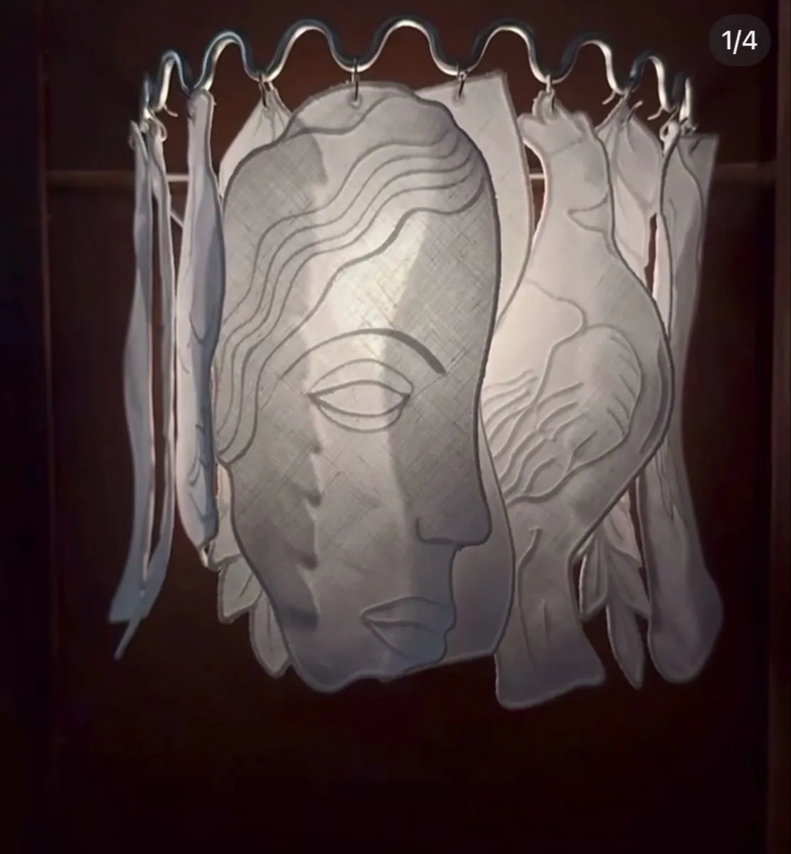 Lit lantern of hanging linen panels cut into a face and a bird, on a wavy metal ring