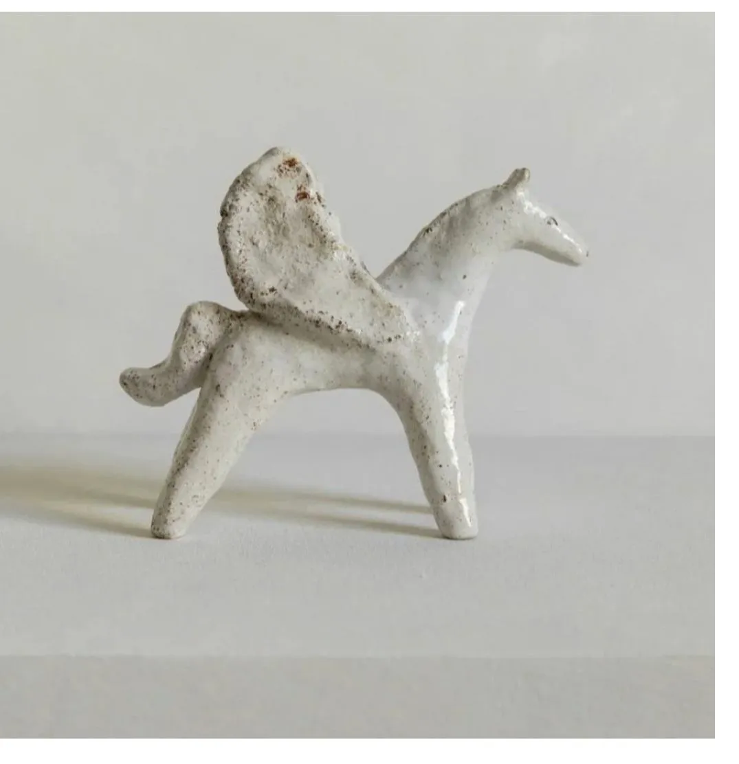 Small white glazed ceramic horse with wings on a plain grey background