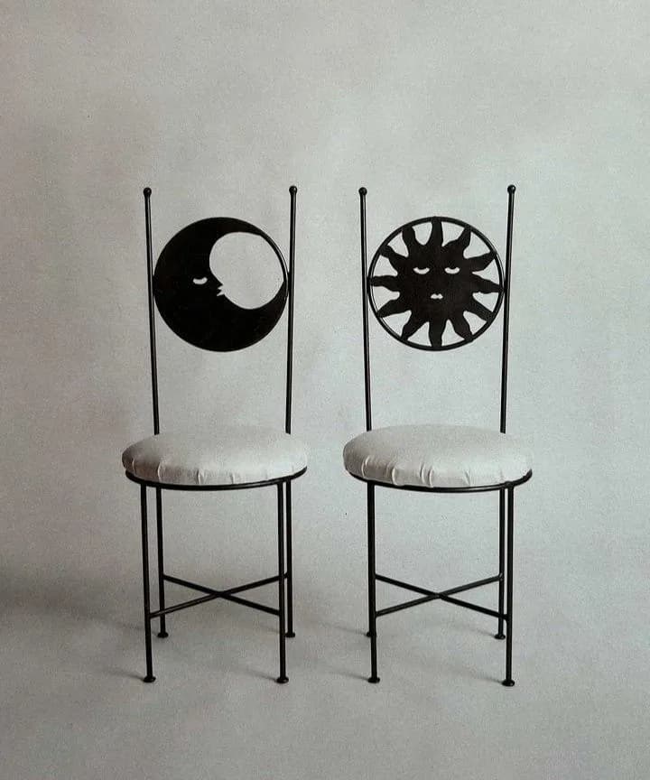 Two black wrought iron chairs with a moon and a sun cut into their tall backs, white round cushions
